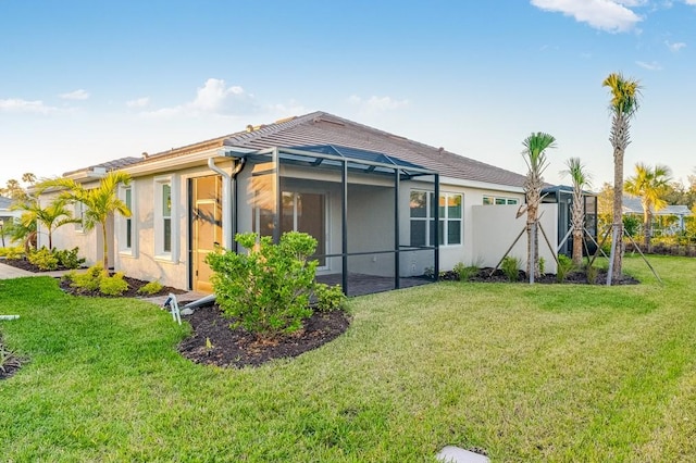 rear view of house with glass enclosure, a lawn, and stucco siding