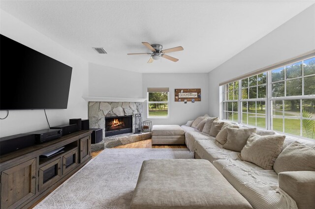 living room featuring ceiling fan, hardwood / wood-style floors, and a stone fireplace