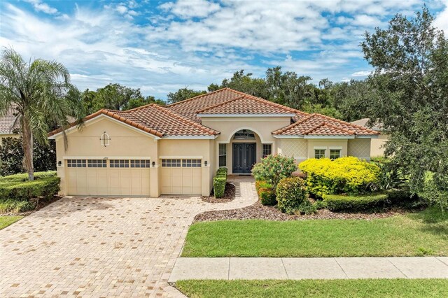 mediterranean / spanish-style house with an attached garage, a tiled roof, decorative driveway, and stucco siding