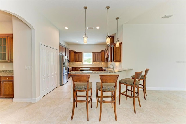 kitchen with pendant lighting, a kitchen breakfast bar, stainless steel refrigerator with ice dispenser, light stone countertops, and kitchen peninsula