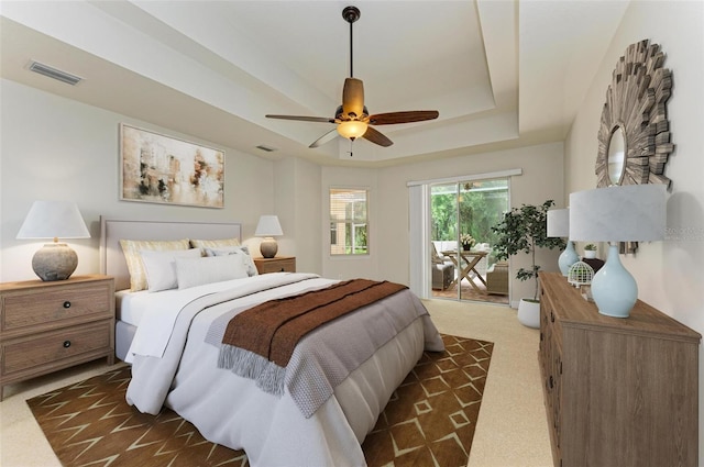 carpeted bedroom featuring access to outside, ceiling fan, and a tray ceiling