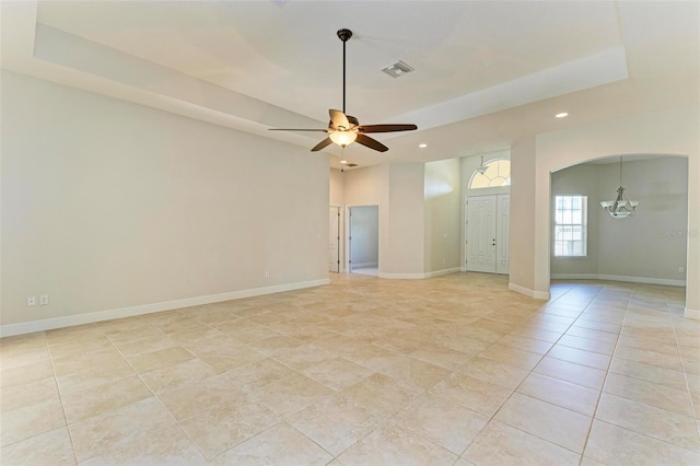 empty room with a raised ceiling, light tile patterned floors, and ceiling fan with notable chandelier