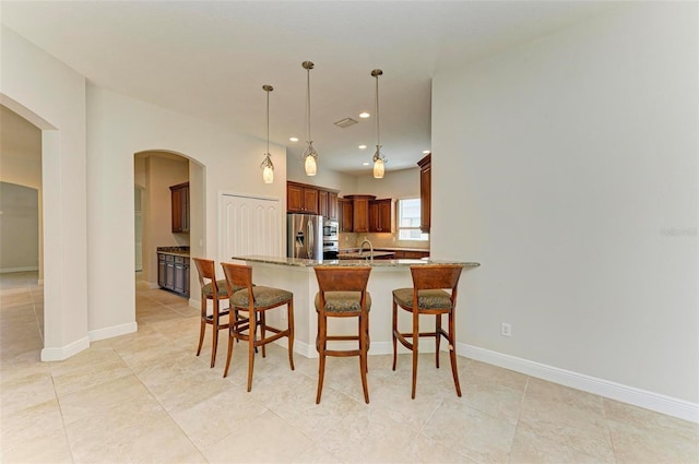 kitchen featuring kitchen peninsula, light stone countertops, stainless steel appliances, sink, and decorative light fixtures