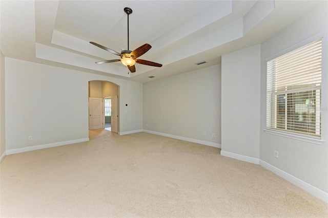 carpeted spare room with a raised ceiling and ceiling fan