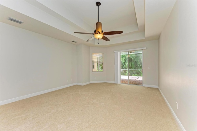 unfurnished room featuring a raised ceiling, ceiling fan, and light colored carpet