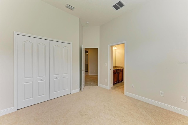 unfurnished bedroom featuring connected bathroom, light carpet, a closet, and a high ceiling