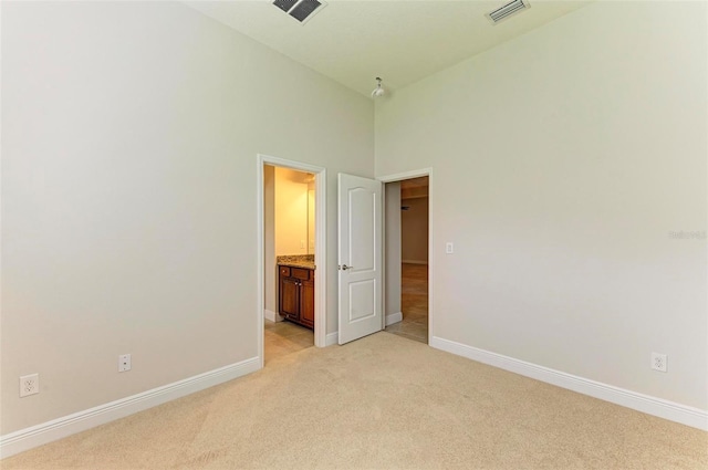 unfurnished bedroom with ensuite bathroom, light carpet, and a high ceiling