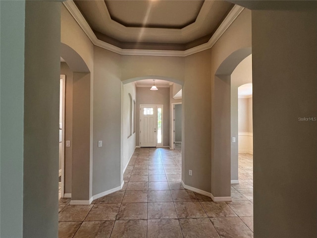 corridor with crown molding, a raised ceiling, a towering ceiling, and light tile patterned flooring