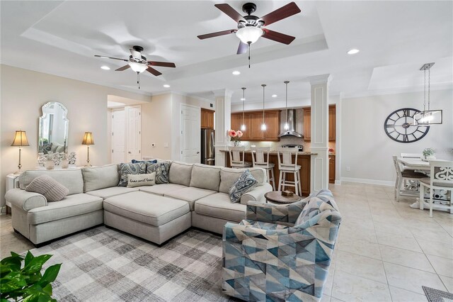 living room with light tile patterned floors, crown molding, ceiling fan with notable chandelier, decorative columns, and a raised ceiling