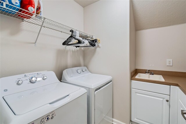 clothes washing area with a textured ceiling, cabinets, washing machine and dryer, and sink