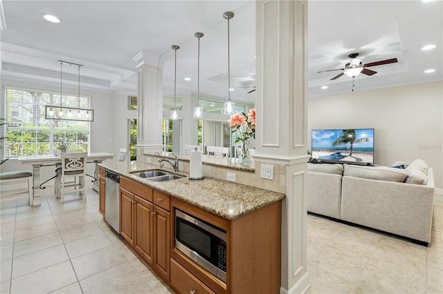 kitchen featuring brown cabinets, decorative columns, appliances with stainless steel finishes, open floor plan, and a sink