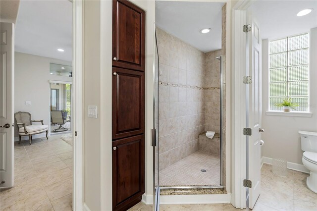 bathroom featuring tile patterned floors, a shower with shower door, toilet, and a healthy amount of sunlight