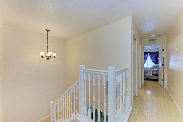 stairway with a textured ceiling, an inviting chandelier, and hardwood / wood-style flooring