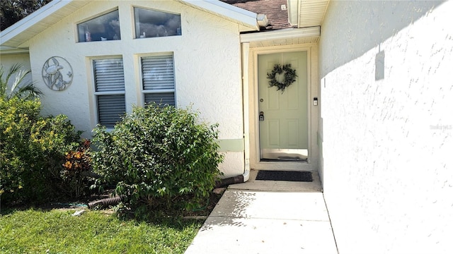 entrance to property with a shingled roof and stucco siding