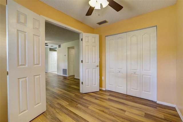 unfurnished bedroom with wood-type flooring, a textured ceiling, a closet, and ceiling fan