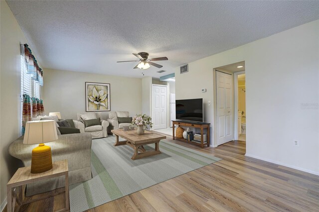 living room featuring ceiling fan, light hardwood / wood-style flooring, and a textured ceiling