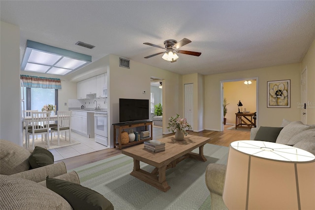 living room with ceiling fan, a textured ceiling, and light wood-type flooring