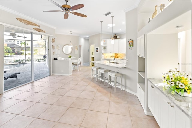 kitchen featuring hanging light fixtures, light stone countertops, sink, ceiling fan, and a breakfast bar