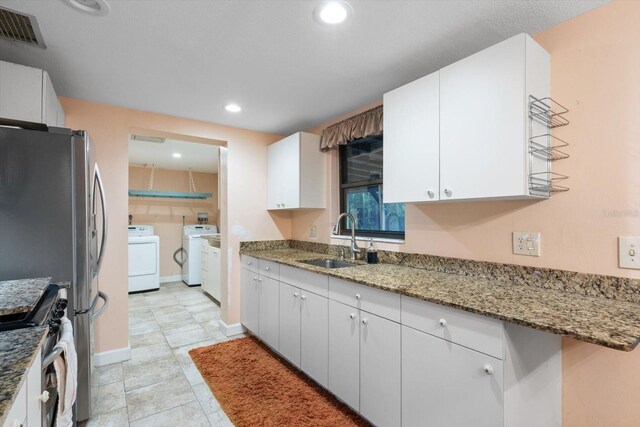 kitchen featuring washing machine and clothes dryer, light stone counters, sink, and white cabinets