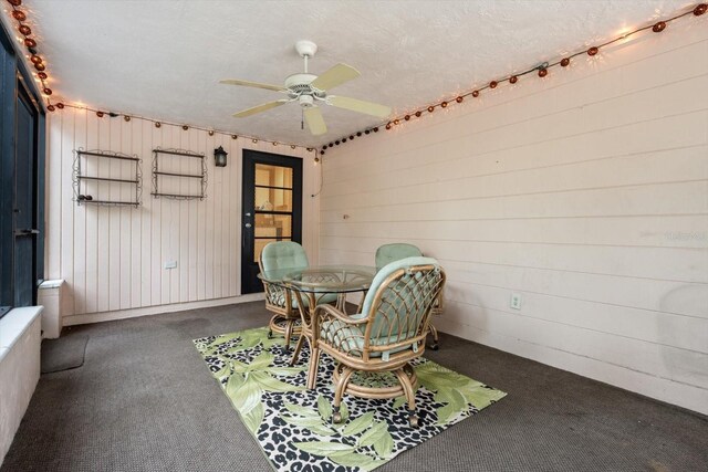 unfurnished dining area with a textured ceiling, wood walls, ceiling fan, and carpet