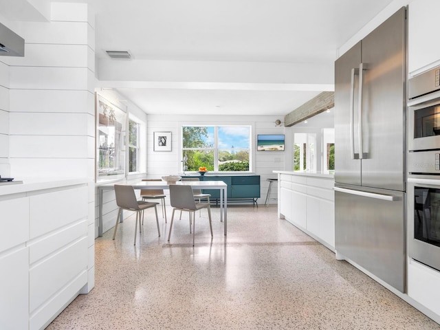 kitchen with white cabinetry, stainless steel fridge, and beamed ceiling