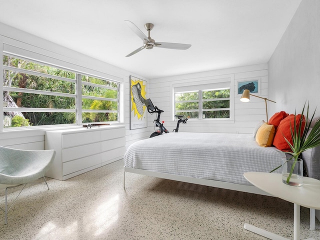 bedroom with ceiling fan, wooden walls, and multiple windows