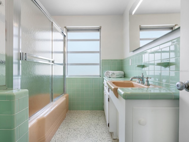 bathroom featuring vanity, combined bath / shower with glass door, and tile walls