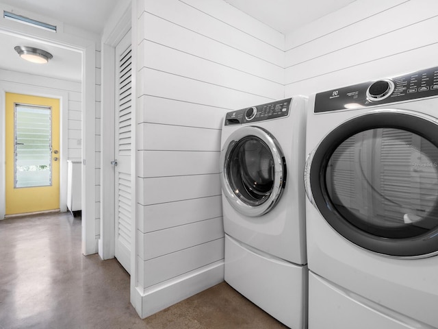 laundry area with washing machine and clothes dryer and wood walls