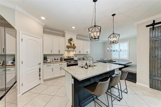 kitchen featuring a kitchen island with sink, stainless steel gas range, sink, and white cabinets