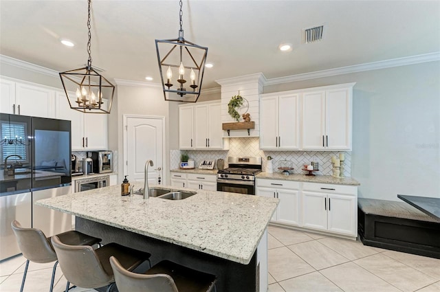 kitchen featuring a kitchen island with sink, stainless steel gas range, a notable chandelier, white cabinetry, and sink