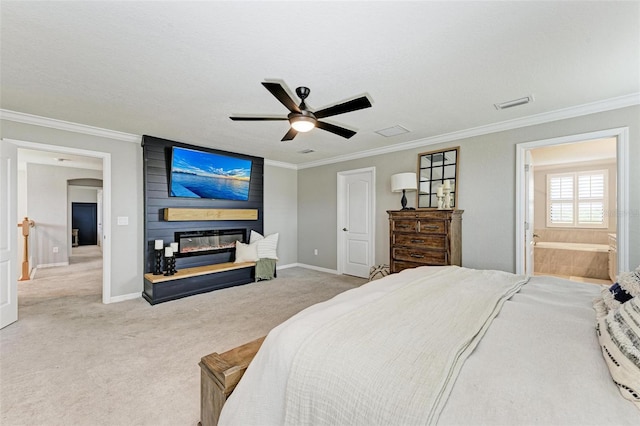 bedroom with a fireplace, crown molding, ensuite bath, light carpet, and ceiling fan