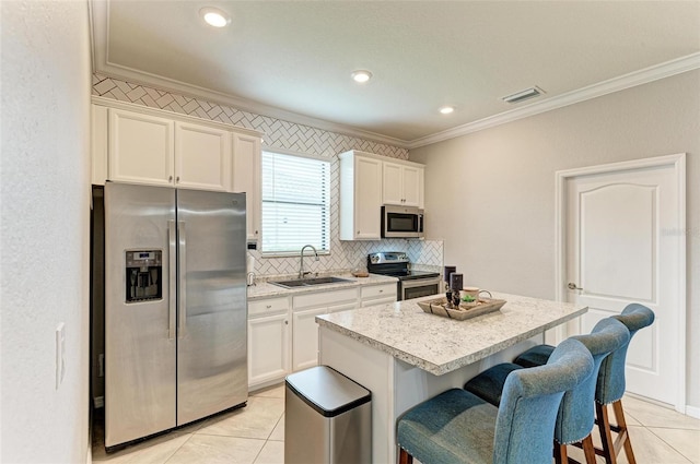 kitchen featuring a kitchen island, a kitchen breakfast bar, appliances with stainless steel finishes, sink, and white cabinets