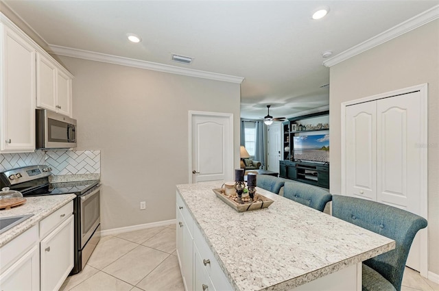 kitchen featuring a breakfast bar area, appliances with stainless steel finishes, crown molding, a center island, and ceiling fan