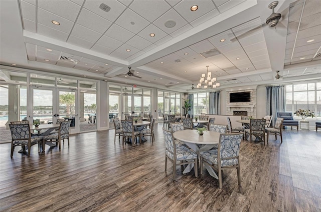 dining area featuring ceiling fan with notable chandelier, dark wood-type flooring, plenty of natural light, and a large fireplace