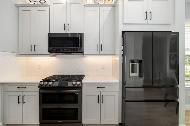 kitchen featuring stainless steel appliances, light stone countertops, decorative backsplash, and white cabinets