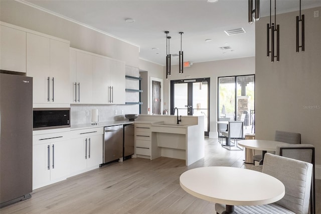 kitchen featuring white cabinets, crown molding, appliances with stainless steel finishes, light hardwood / wood-style floors, and pendant lighting