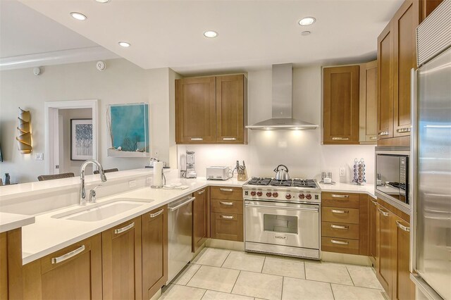 kitchen featuring built in appliances, wall chimney exhaust hood, light tile patterned floors, kitchen peninsula, and sink