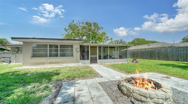 rear view of property with an outdoor fire pit, a sunroom, a lawn, and cooling unit