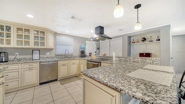 kitchen with cream cabinetry, decorative light fixtures, light stone counters, island exhaust hood, and appliances with stainless steel finishes