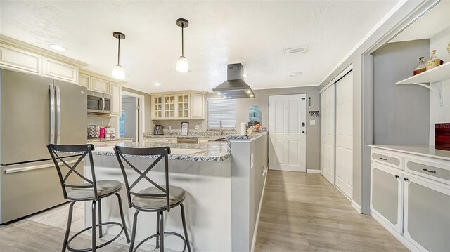 kitchen with light stone countertops, cream cabinets, appliances with stainless steel finishes, island exhaust hood, and hanging light fixtures