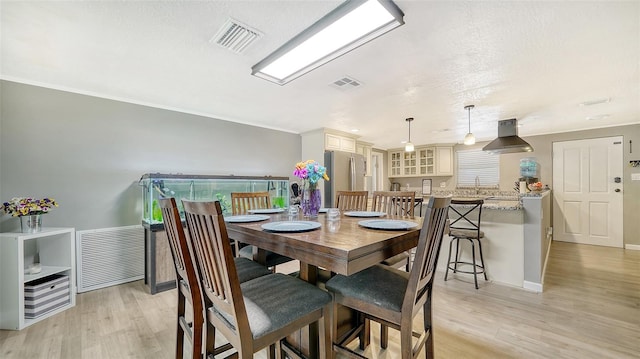 dining space featuring light wood-type flooring, ornamental molding, and a textured ceiling