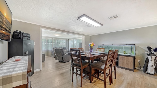 dining room featuring a textured ceiling, light hardwood / wood-style flooring, and ornamental molding