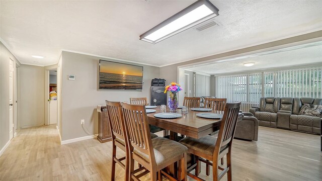 dining area featuring light wood-type flooring, a textured ceiling, and ornamental molding