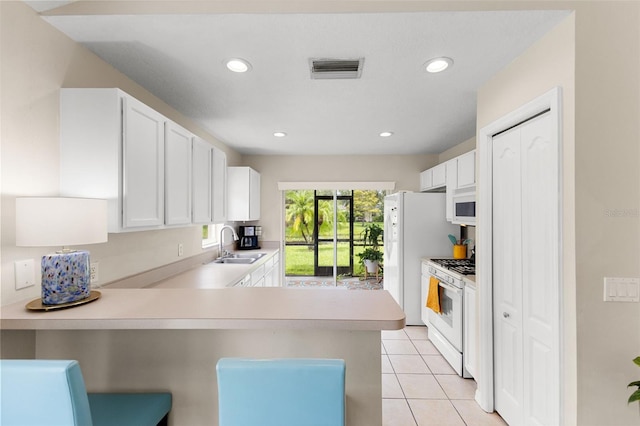 kitchen with white appliances, light tile patterned floors, kitchen peninsula, sink, and white cabinets