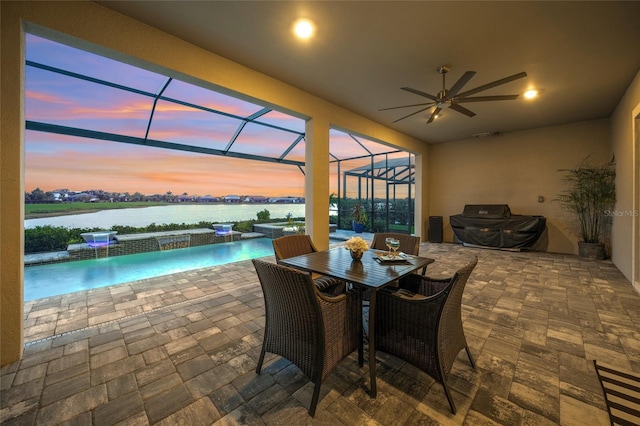 patio terrace at dusk featuring pool water feature, ceiling fan, a water view, and a lanai