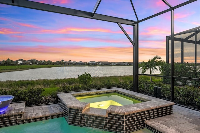 pool at dusk with glass enclosure, a water view, and an in ground hot tub