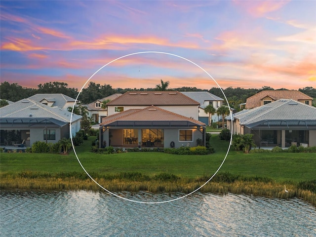 back house at dusk with a water view and a yard