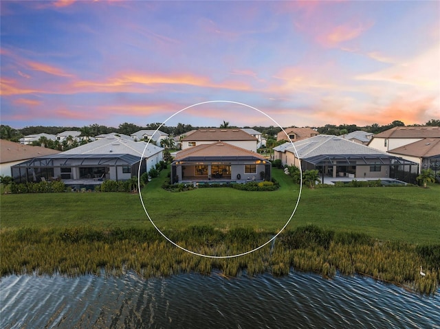 back house at dusk with a lawn, glass enclosure, and a water view