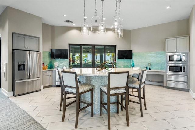 kitchen featuring a center island, hanging light fixtures, tasteful backsplash, gray cabinets, and appliances with stainless steel finishes