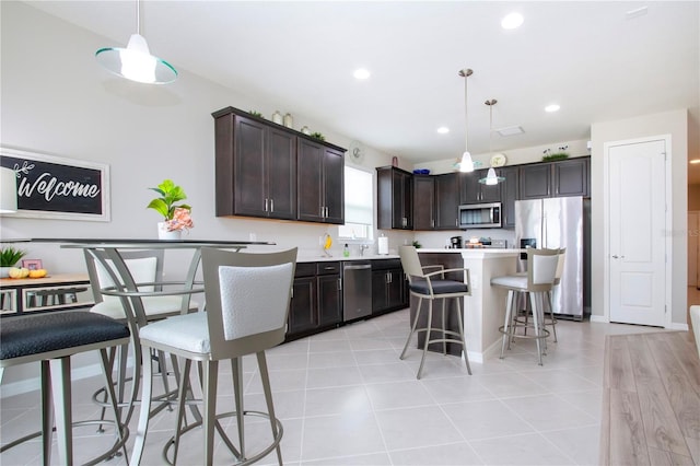 kitchen featuring appliances with stainless steel finishes, dark brown cabinets, a breakfast bar, and hanging light fixtures